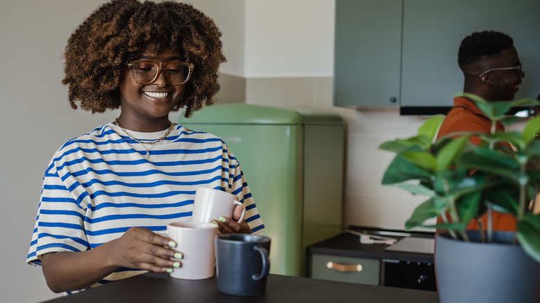 Woman looking at three mugs on the countertop in a modern kitchen.