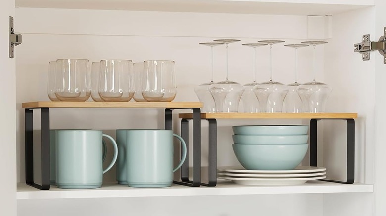 Wooden shelf risers in a cabinet holding glasses with dishes beneath them