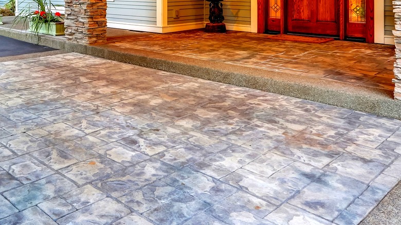 A driveway surface covered in rust and dirt spots in the foreground with an elevated front entryway in the backgbround