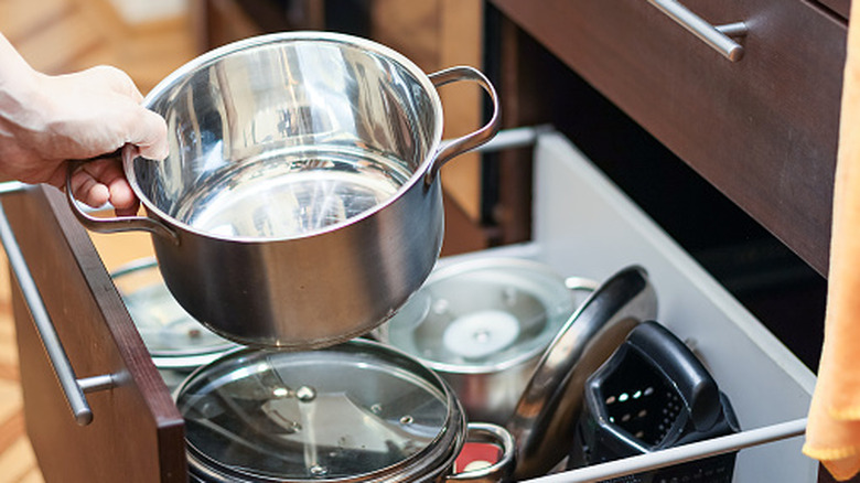 Offscreen person stacking pot on top of messy cabinet