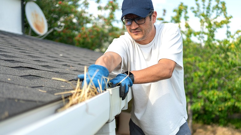 A person on a ladder cleaning gutters