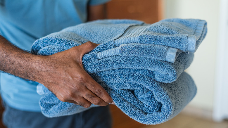 A person holding a stack of clean, folded blue towels