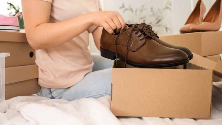 person sitting on bed putting shoes into box for storage