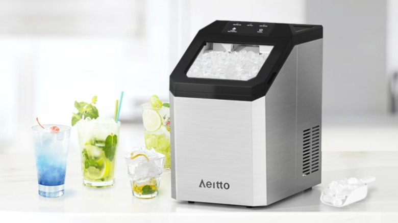 The Aeitto ice maker sitting on a countertop with several drinks and a scoop of ice next to it