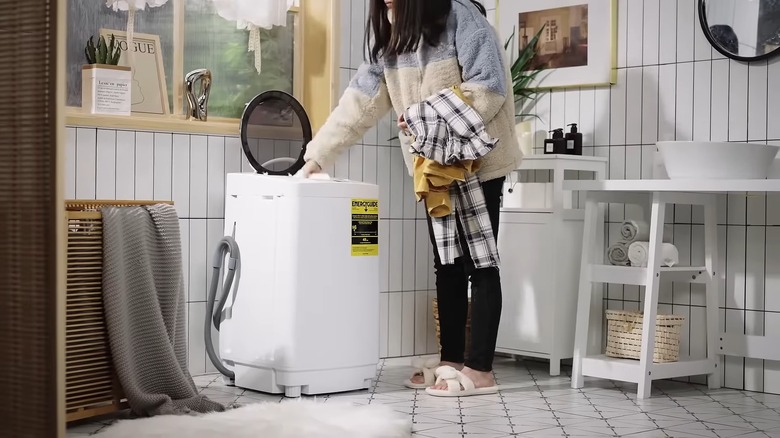 Person adding dirty clothes to a portable washing machine.