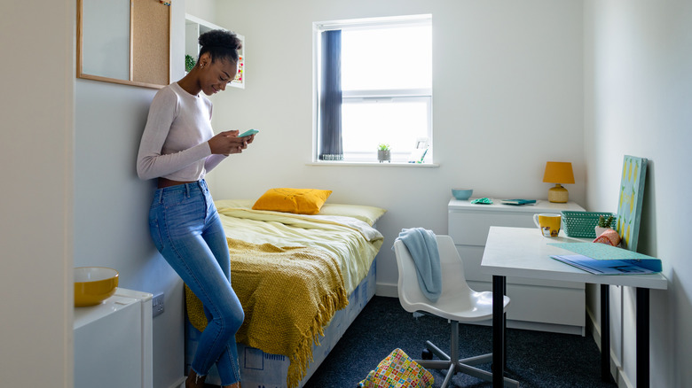 Woman standing in a small bedroom without much storage space.
