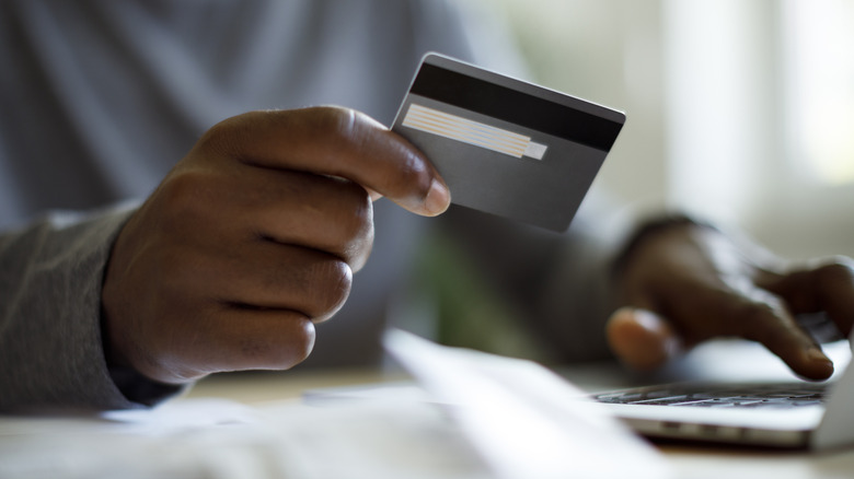 A person holding a credit card and typing in information on their computer