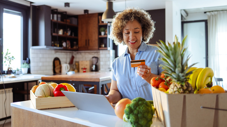 A woman holding her credit card while online shopping in a kitchen