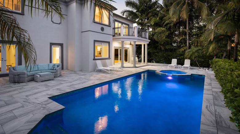 The backyard of a luxurious home in Florida with a deep blue pool illuminated in the evening.