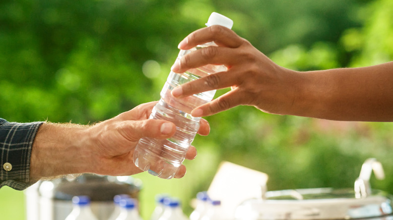 Hand handing plastic water bottle to another hand