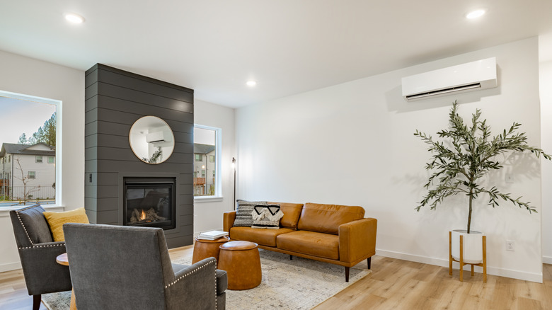 A modern-style living room with white walls and tan and dark gray furniture with a dark gray fireplace.