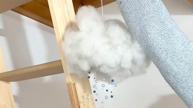 A person hangs a raincloud DIY project from a wooden beam