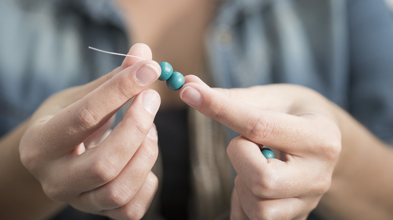 A person puts blue beads onto string