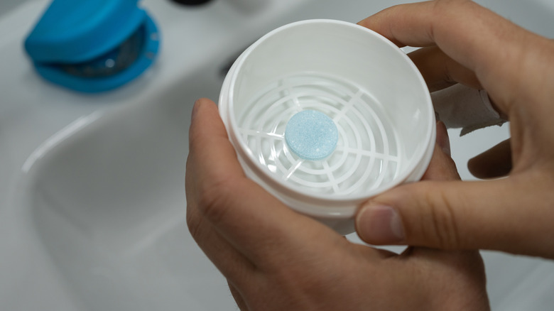 A man holds a denture tablet over the bathroom sink.