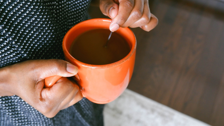 A woman stirs coffee in a mug that she's holding in her hand.