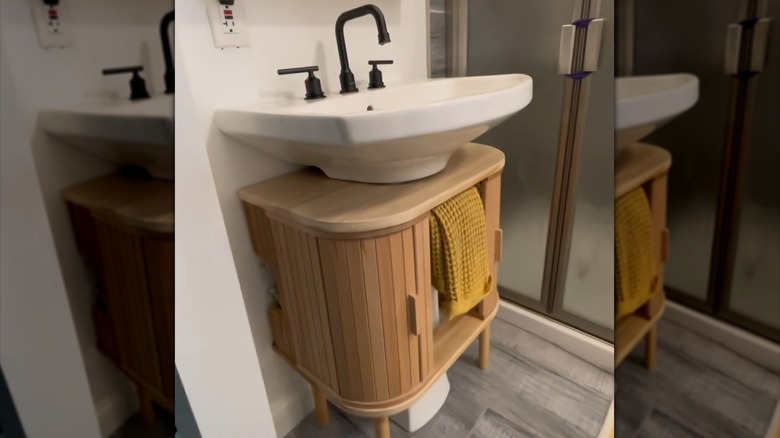 Wooden cabinet around a bathroom pedestal sink with yellow waffle towel hanging from a bar inside