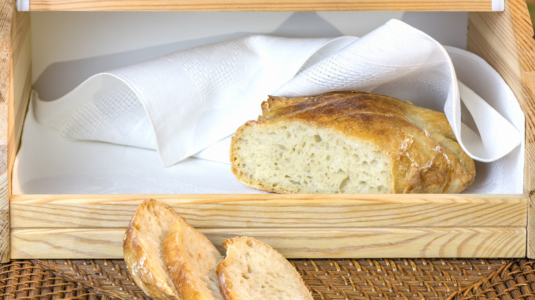A wooden bread box with cloth and fresh sliced bread