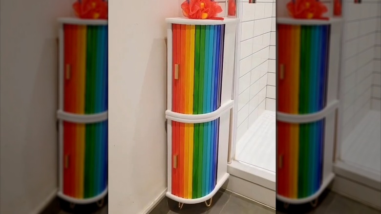 Wood cabinet, made from bread bins, painted with each slat a different to create a rainbow effect sits next to a white tiled shower in a bathroom