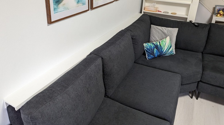 White picture ledge hung upside down over the edge of the couch to make a ledge for drinks