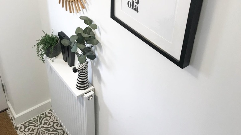 Radiator shelf made of a flipped picture ledge in a hallway near art