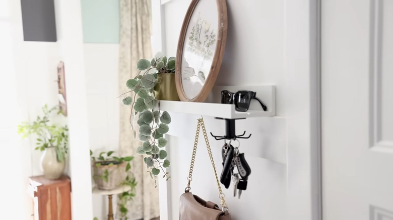 Foyer of a home with a white picture ledge shelf turned into a wall shelf with framed print, plant, sunglasses, and hooks