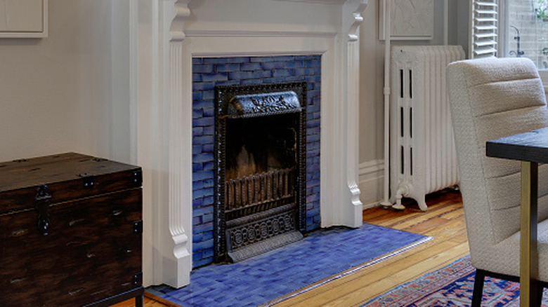 A historic fireplace with white painted wood on the sides, blue tiles with multiple shades, and a cast iron door.