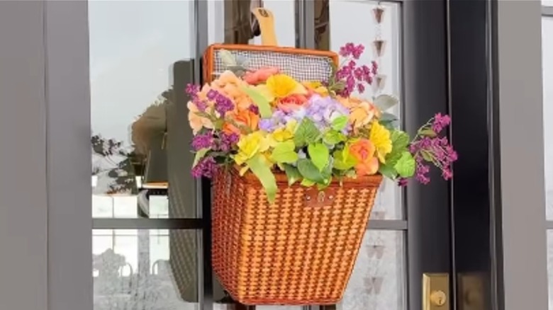 A picnic basket filled with faux flowers hangs on a front door.