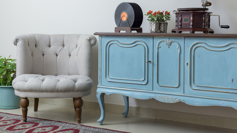 Blue vintage console with antique decor on top next to a grey chair