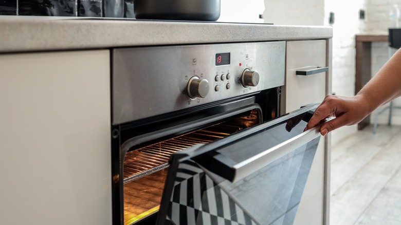 A hand opens a hot oven with a light on