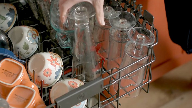 Someone putting a tall glass on the bottle washer jet in a dishwasher