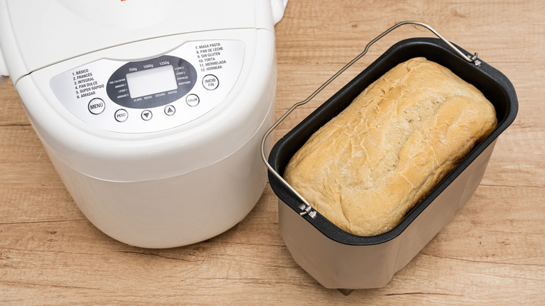 Loaf of bread sitting in its container next to a breakmaking machine