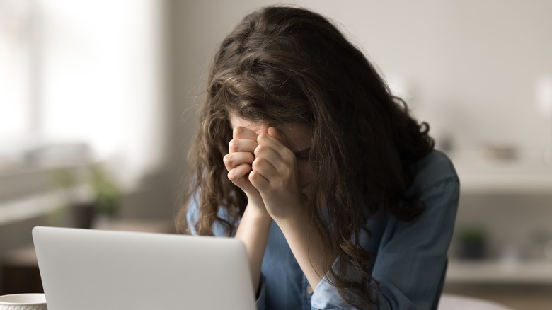A young woman prays while working on a computer