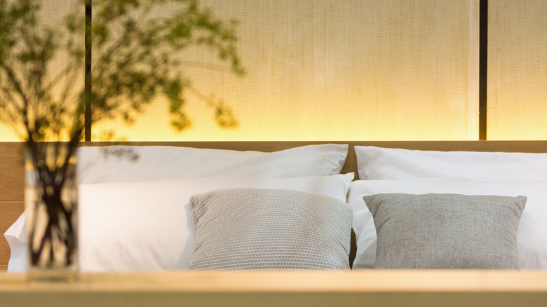 close up of elegant large bed with cream colored bedding, green throw pillows and dark wood headboard
