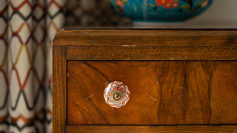 A colorful ceramic knob on a wooden chest of drawers