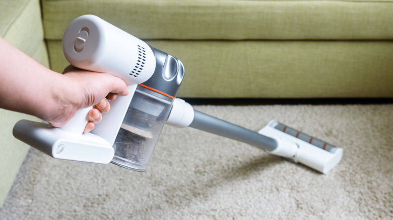 Hand holding cordless stick vacuum to clean carpet