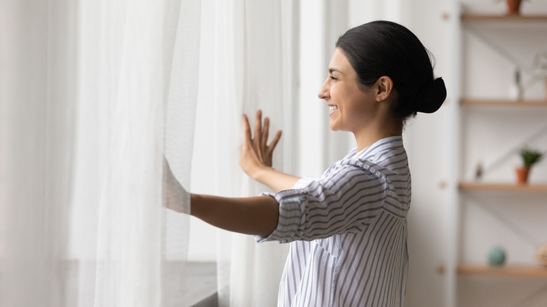 smiling woman opening curtains
