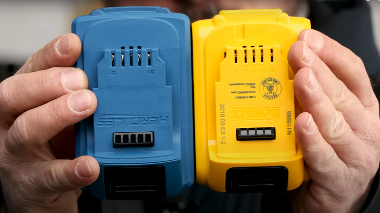 A man's hands holding up a DeWalt battery next to a Hercules battery