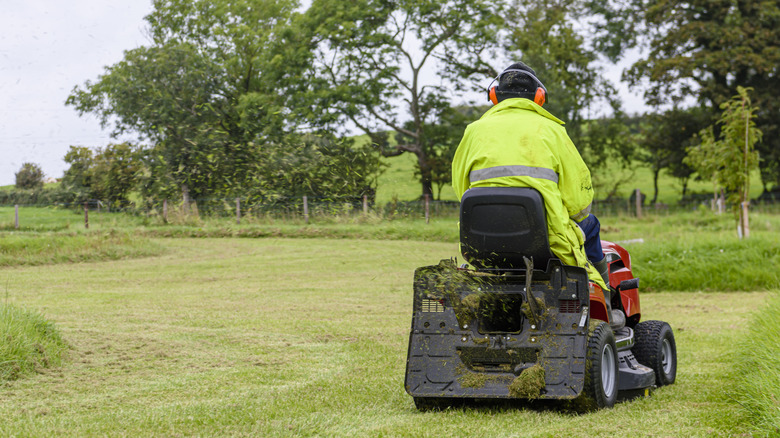 A man in a high-visibility jacket mowing a lawn with a riding mower