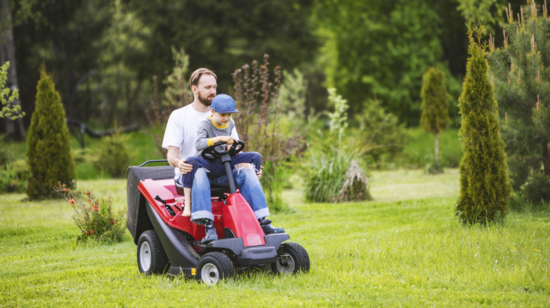 A father and son mowing the grass together on a riding lawn mower