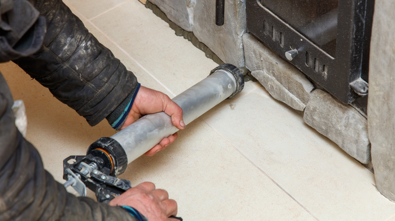 A man with a metal caulk gun applying sealant to a fireplace