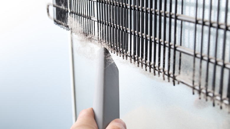 Person cleaning backside of fridge coils with vacuum