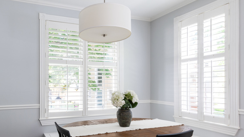 Windows with white wood shutters above a table with flowers