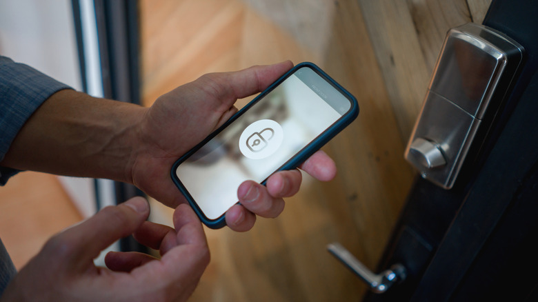 Close-up on a man opening the door of his house using a home automation system on his cell phone.