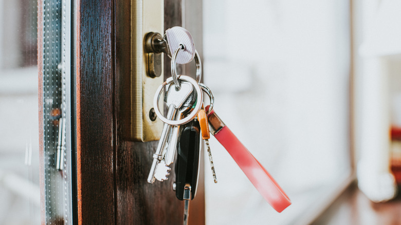 Bunch of keys on a keyring, including a car key fob, hanging on the lock of a thick, composite glass door.