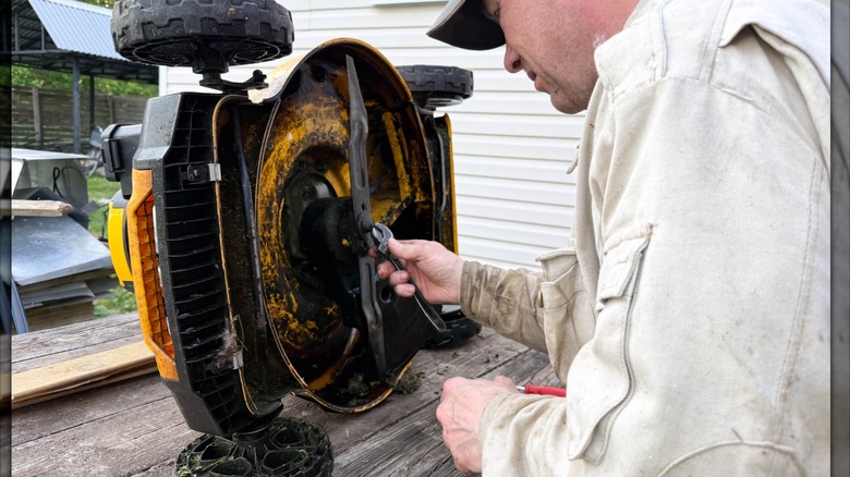 A man repairs a lawn mower on a wooden table