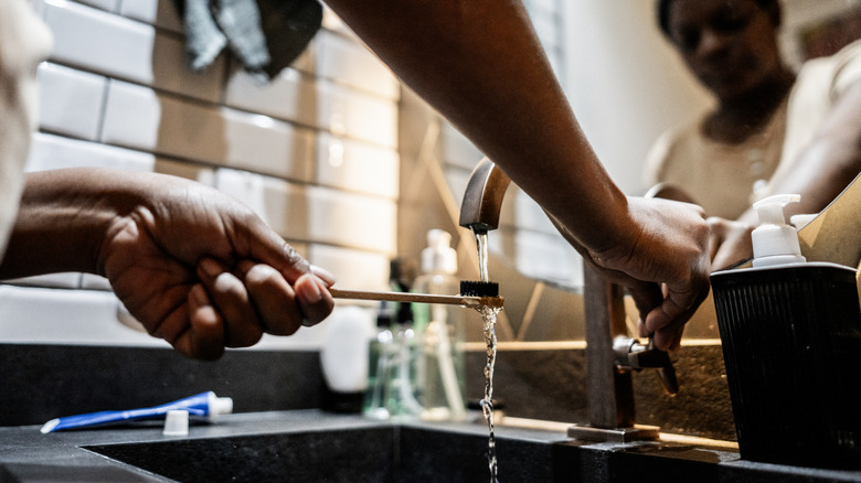 Person rinsing toothbrush in bathroom sink