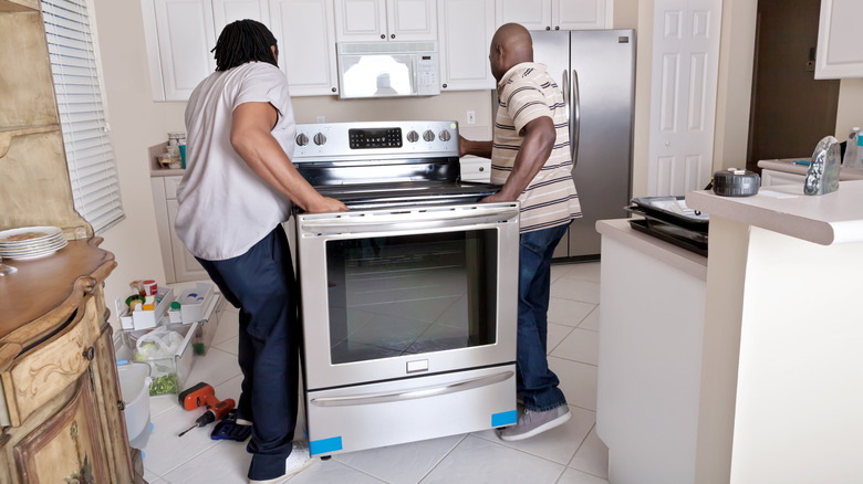 two men installing a brand-new range in a kitchen