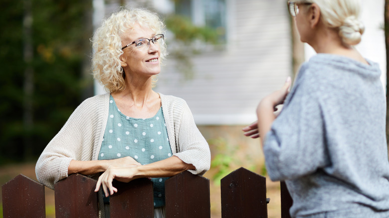 A woman speaks to her neighbor over the fence