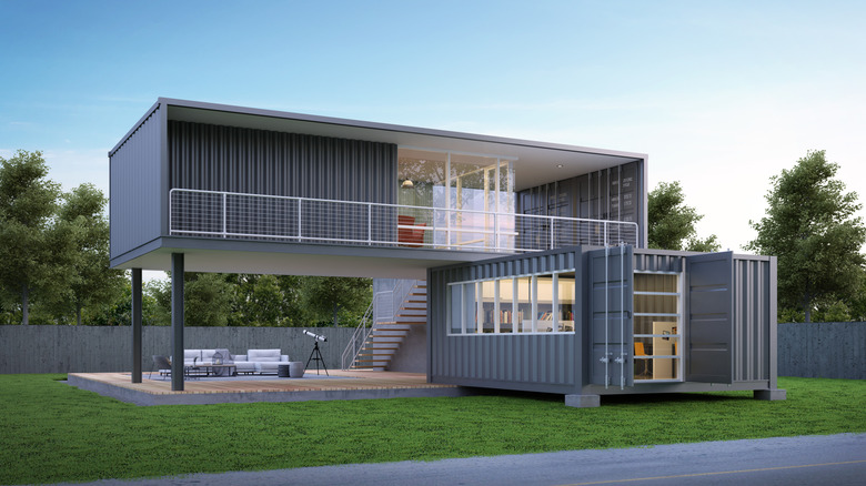 Two gray shipping containers at an angle to each other with windows and balconies.