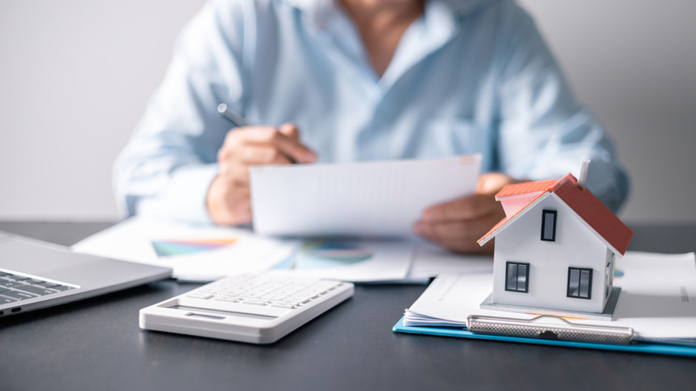 person holding papers with calculator and home miniature for home buying or selling